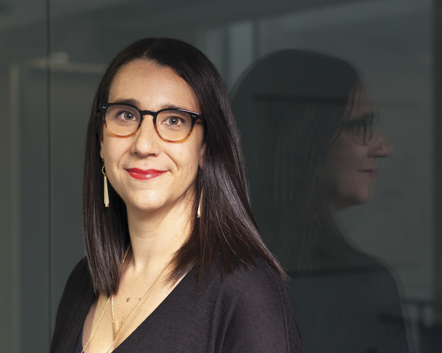 Portrait of a woman with long, dark hair and glasses, smiling at the camera [Anne McGuire].